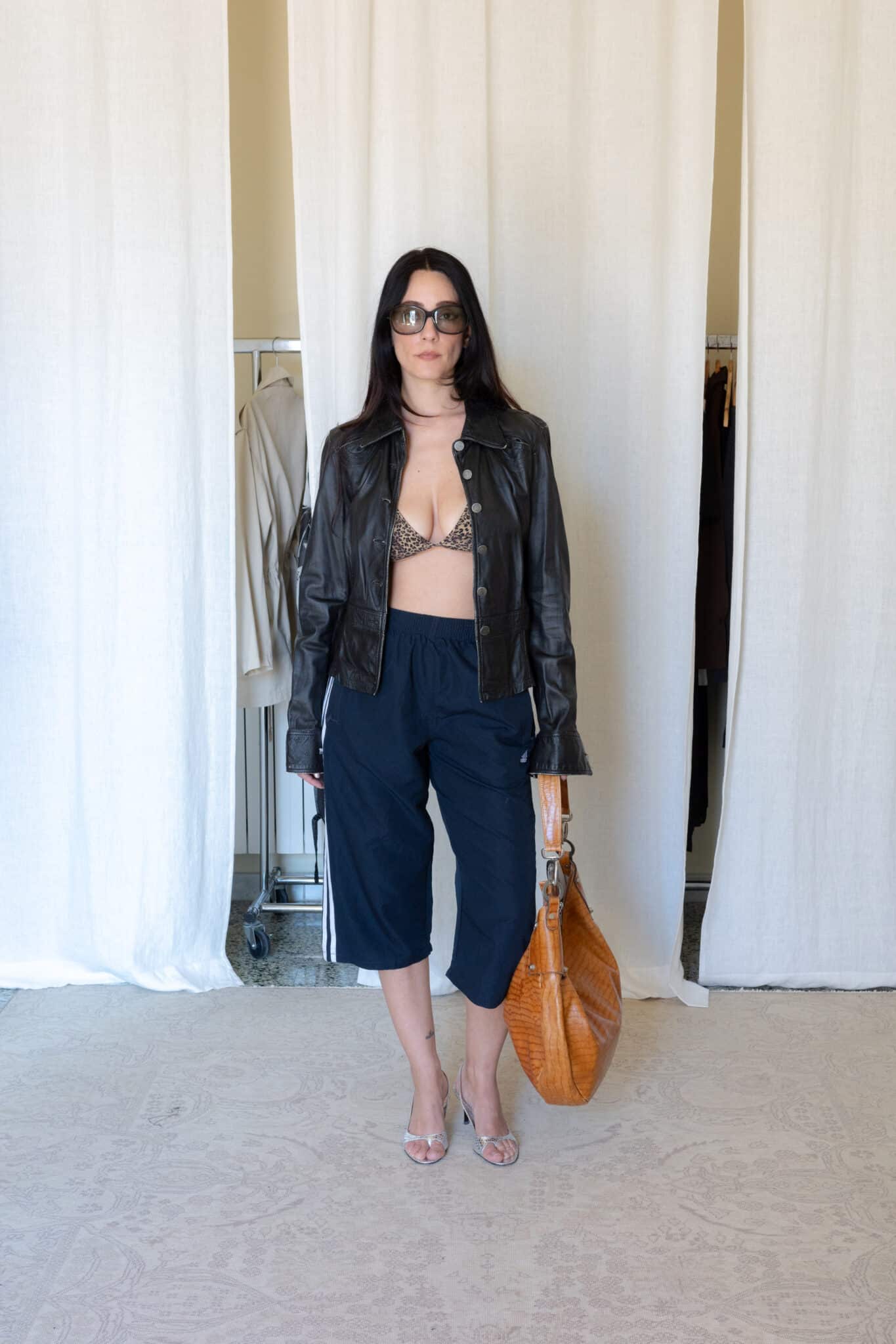 Black fitted leather jacket styled with navy Adidas capri pants, silver heels and oversized woven leather bag
