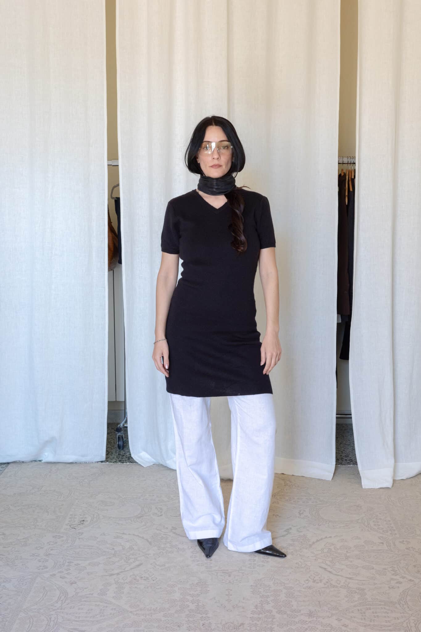 Black fitted short sleeve knit dress layered over wide white linen trousers with pointed black heels and a sheer black scarf.