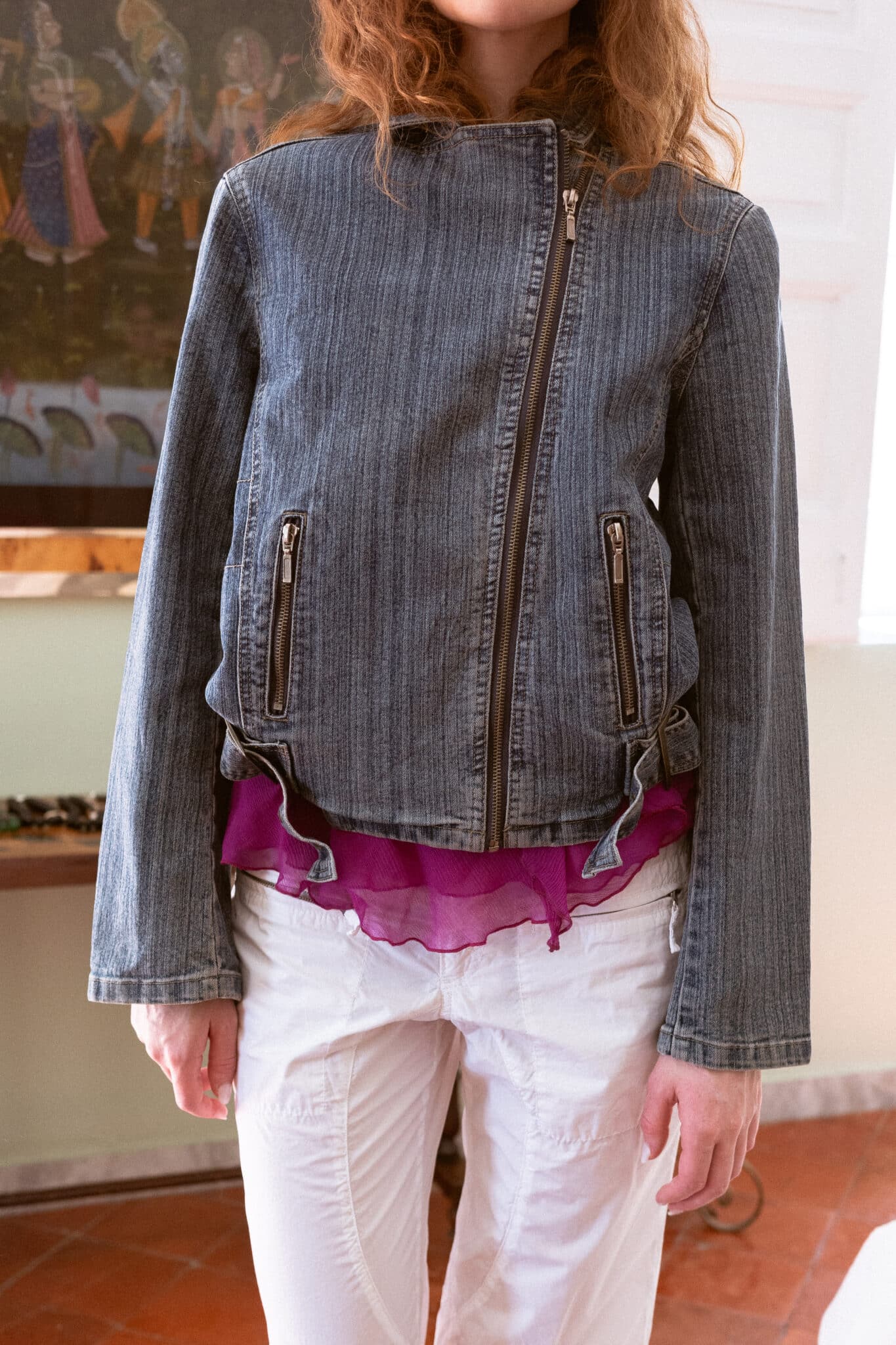 Blue denim jacket with an asymmetric front closure, zip pockets, and adjustable waist tabs.