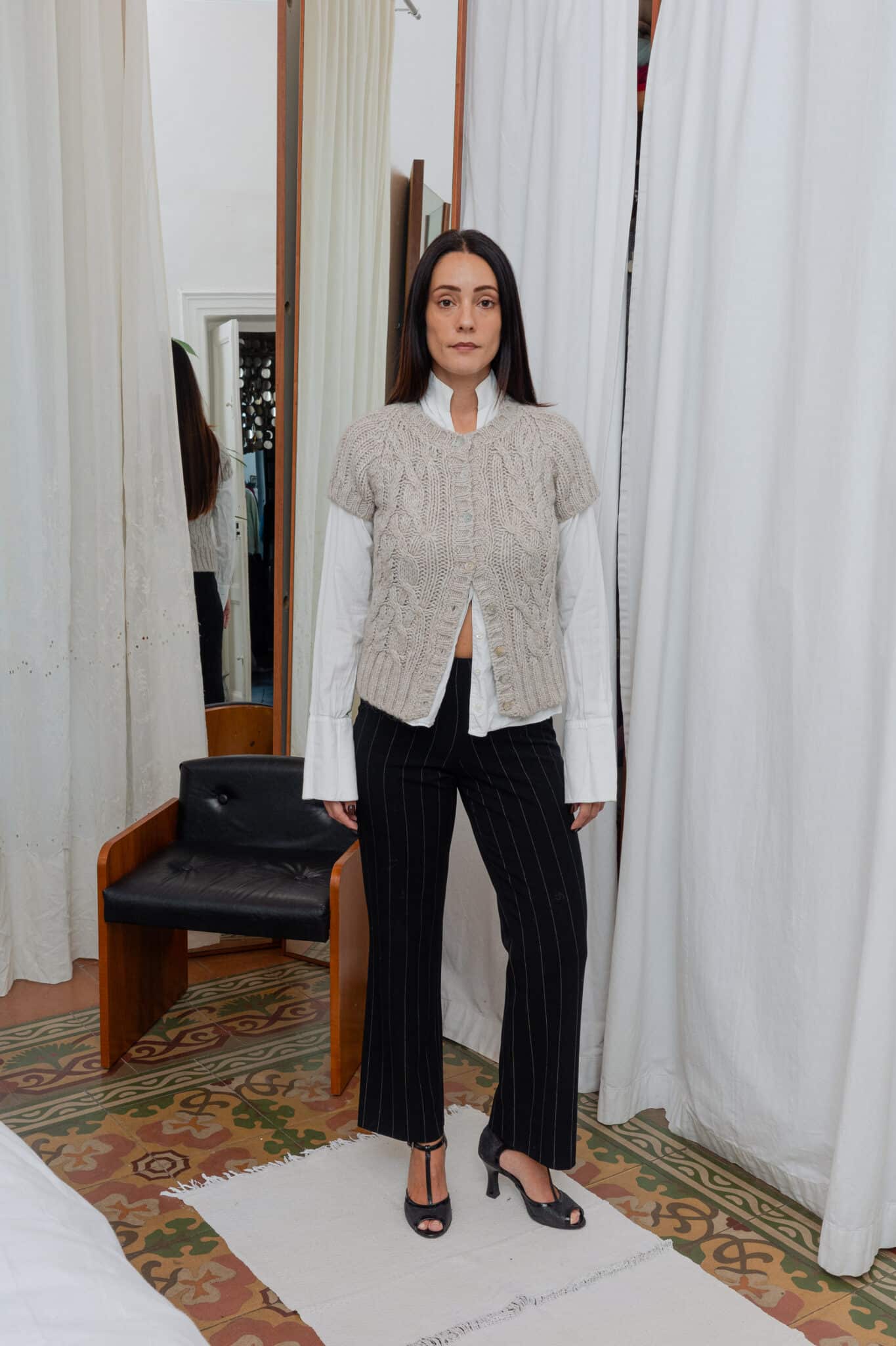 Front view of outfit featuring beige knit vest layered over white shirt with black pinstripe trousers.