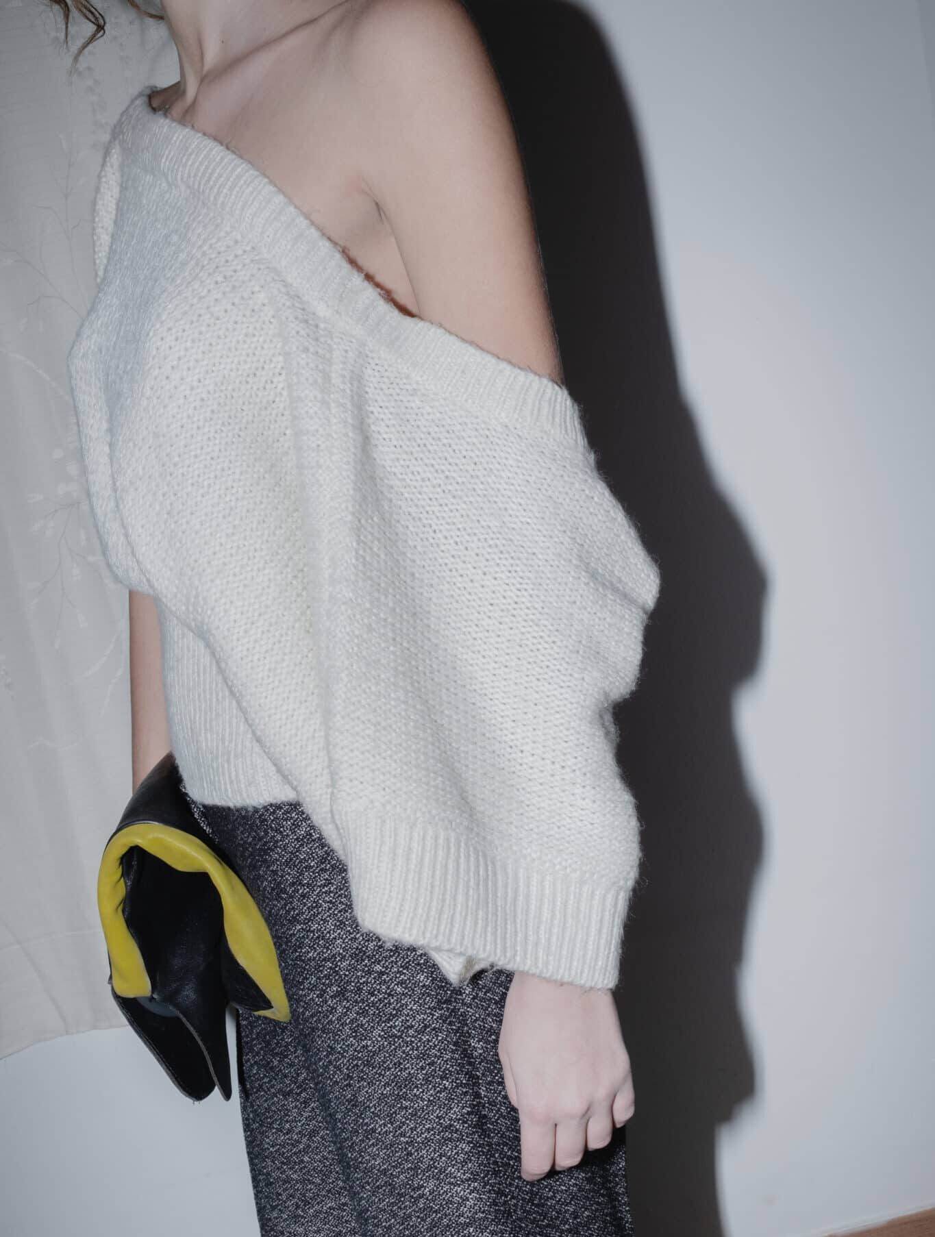 draped knit top in cream worn with heather-grey trousers.