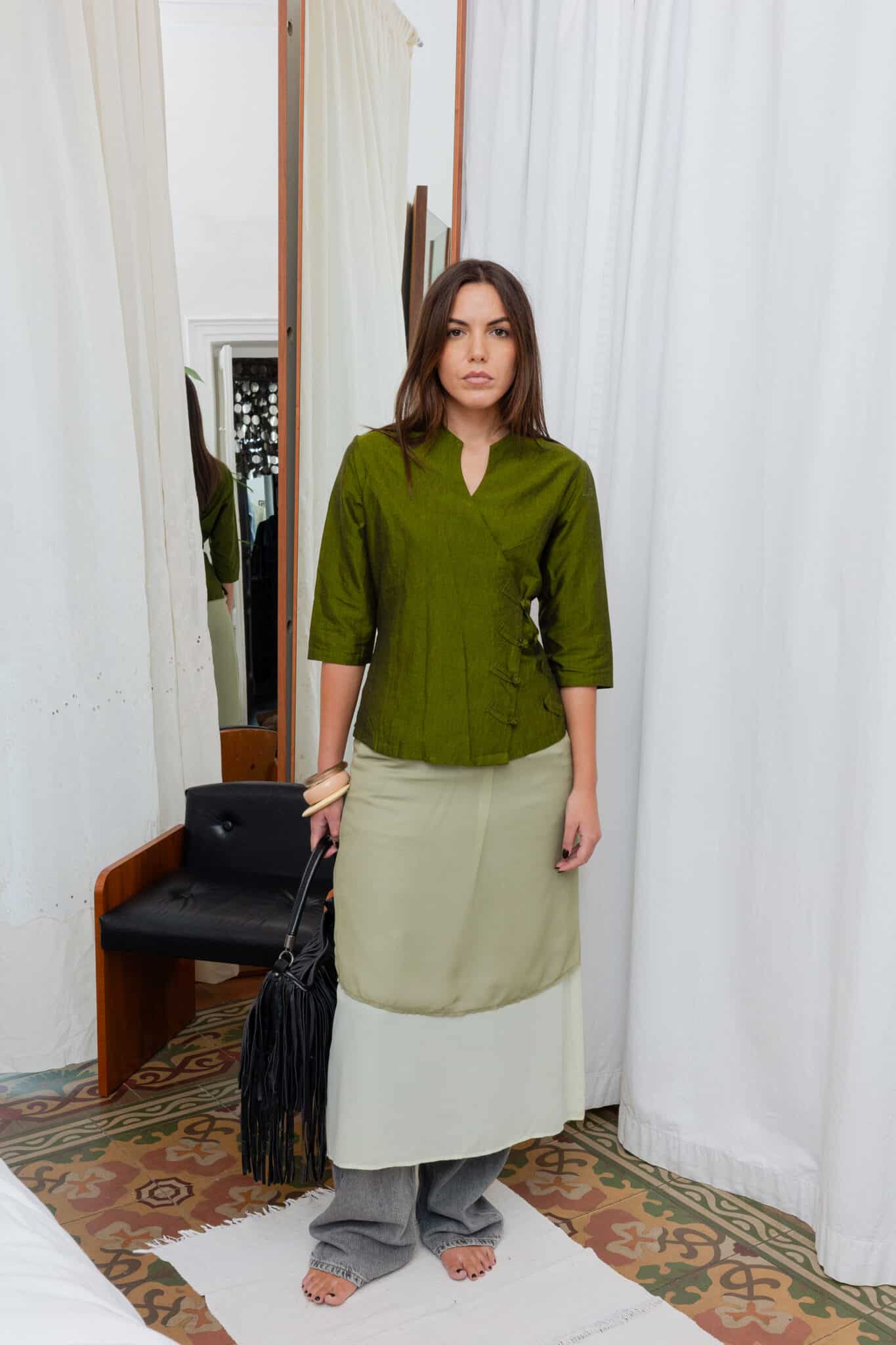 Back view of green wrap top and layered light green skirt styled with grey pants.