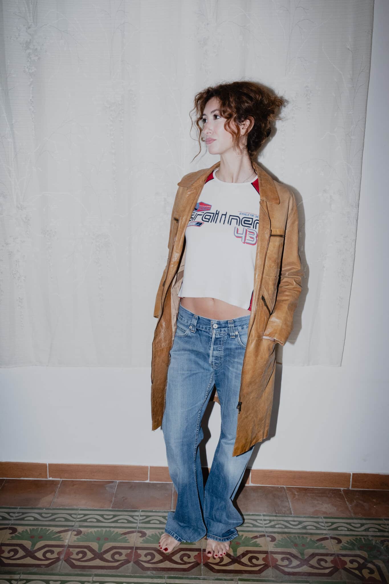 Model iført brun lædercoat, grafisk long-sleeve og let falmede Levis bootcut jeans.