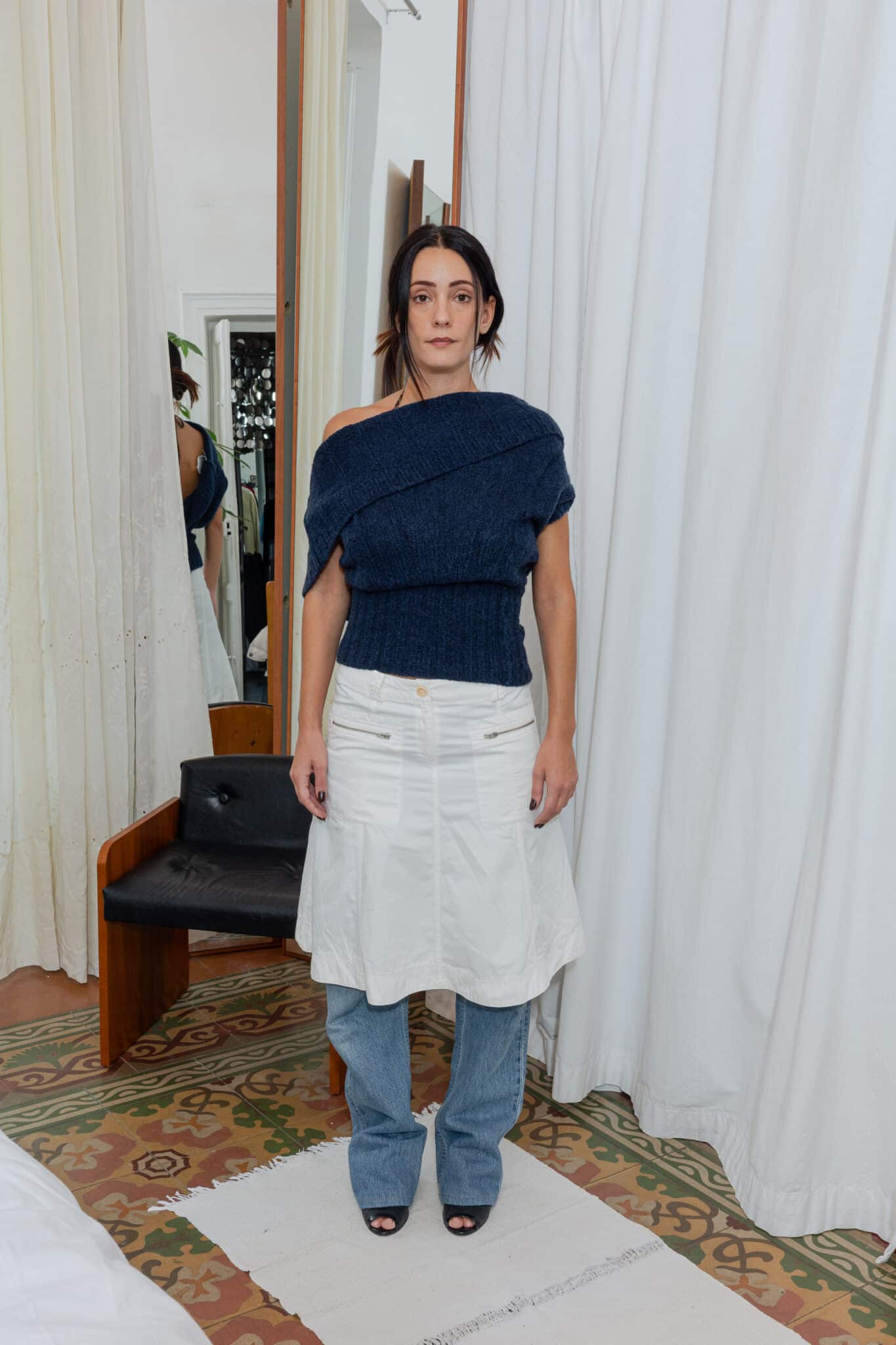 Front view of outfit featuring navy off-shoulder knit top styled with white skirt and jeans.