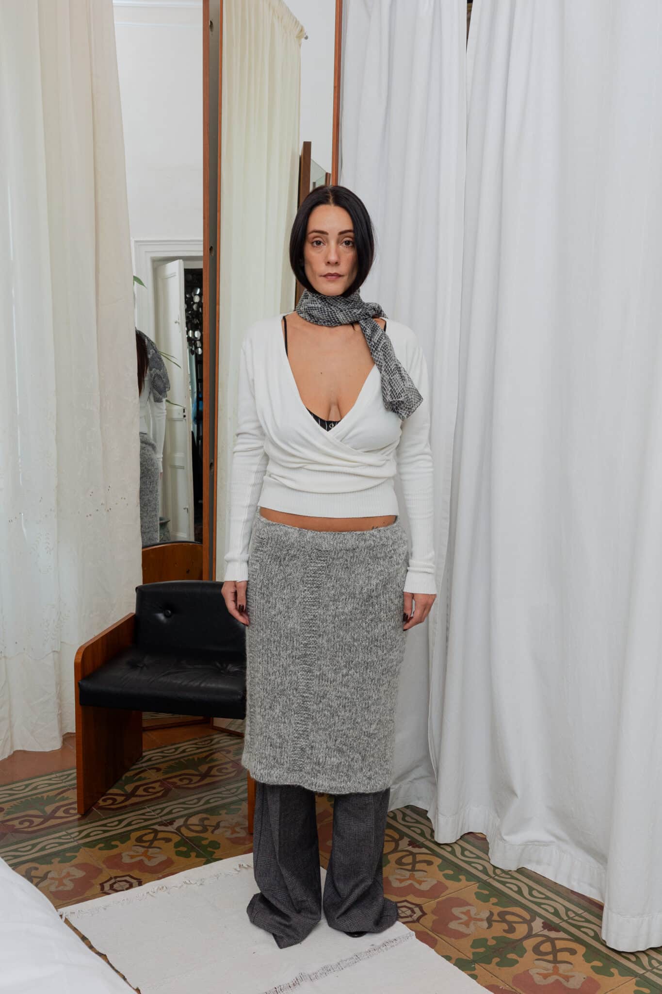 Front view of outfit featuring white wrap top, grey knit skirt layered over grey trousers, and printed scarf.